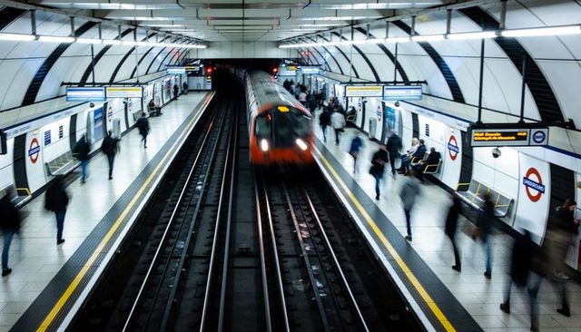 Blurred london underground train approaching platform during rush hour, commuters moving