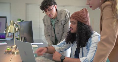 Diverse team collaborating around laptop in modern office, brainstorming digital project