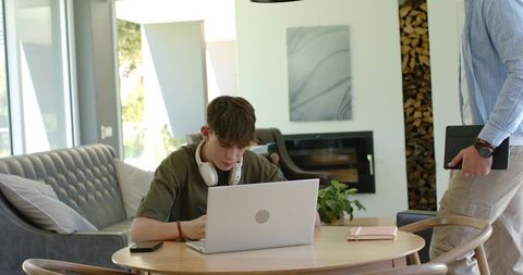 Teen studying at home with laptop while parent holds tablet in contemporary living room