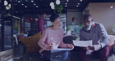 Coworkers reviewing documents in modern office lounge collaborating over coffee