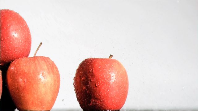 A close-up of fresh Gala apples glistening with water droplets against a white background. The super slow motion captures the detail of droplets, highlighting the freshness of the fruit. Ideal for healthy eating campaigns, grocery advertisements, and blog content about fresh produce.