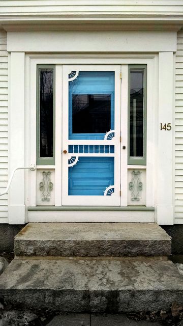 Bright blue front door with intricate decorative trim on white framework, along with granite porch steps leading to the entrance. Useful for home improvement, real estate listings, and architectural studies. Provides a welcoming and distinctive aesthetic for suburban homes.