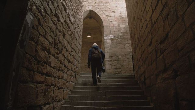 Climbing beanie-clad man ascending stone steps toward lit archway in historic fortress