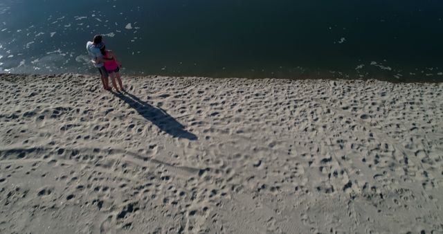 Aerial view of a couple standing on a sandy beach by the shoreline. The man and woman are enjoying a relaxing moment near the water. This could be used for vacation promotions, relaxation and bonding themes, or outdoor and nature-related content.