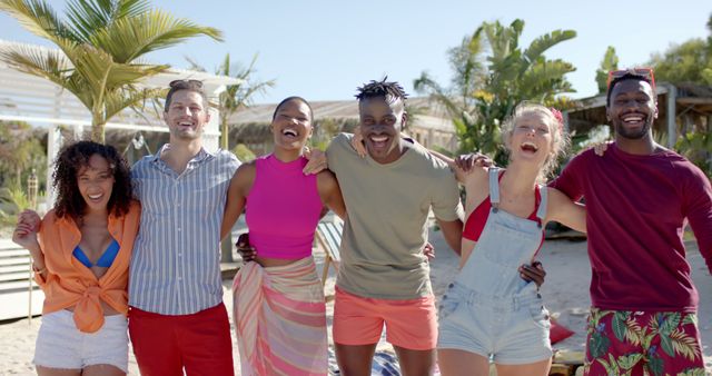 Portrait of happy diverse group of friends embracing on beach with beach house. Vacation, free time, summer and friendship.