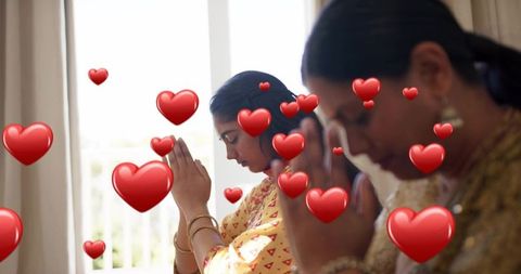 Indian mother and daughter praying palms together wearing yellow sarees and gold jewelry