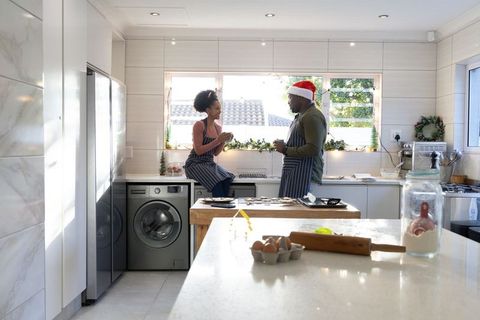 African american couple baking christmas cookies in sunlit modern kitchen, man in santa hat
