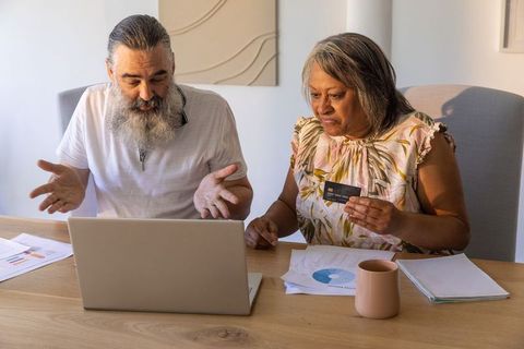 Senior couple reviewing finances online holding credit card while budgeting at home
