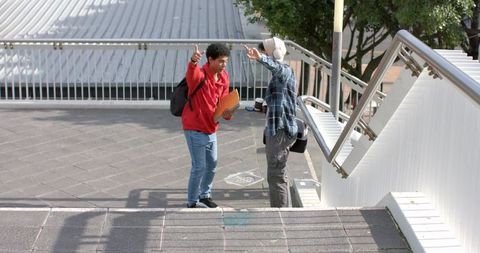 Diverse young men pointing and talking on urban overpass stairway with folder and coffee