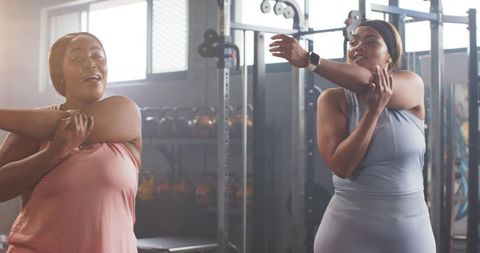 Two women stretching shoulders at gym before strength training and kettlebell session