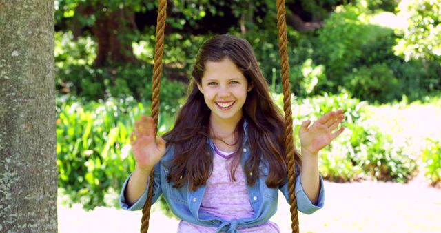 Smiling girl enjoying a sunny day on a swing in a park with lush green surroundings. Perfect for use in articles about childhood, outdoor activities, happiness, family outings, and summer fun.