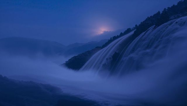 Moonlit cascade flowing through misty mountain valley during blue hour long exposure