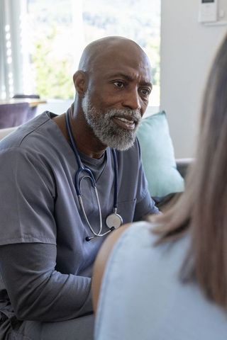 Senior clinician consulting patient during home visit providing compassionate care with stethoscope