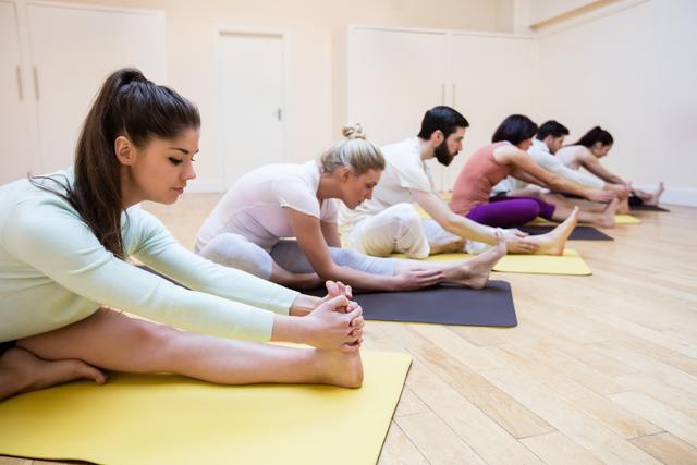 Group performing stretching exercises in a fitness studio, perfect for illustrating concepts of teamwork, physical fitness, and wellness. Ideal for use in fitness blogs, workout guides, wellness articles, and promotional materials for gyms or yoga studios.