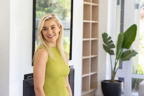 Smiling blonde woman standing by modern fireplace wearing sleeveless lime-green dress