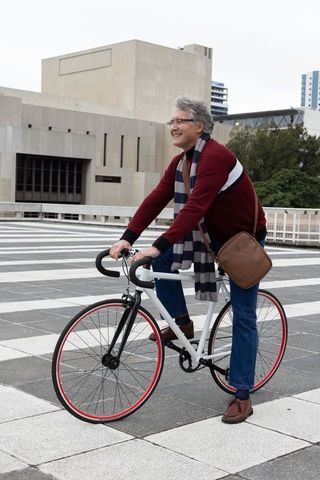 Mature man cycling through urban plaza wearing maroon sweater and carrying leather satchel