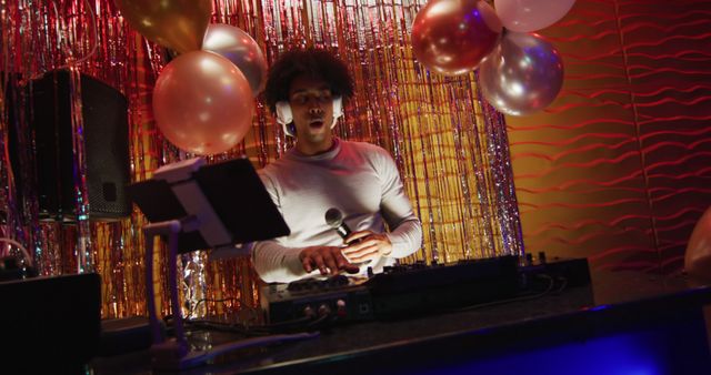 Image of happy african american male dj playing music, dancing and using microphone at a nightclub. Fun, inclusivity, going out and party concept.