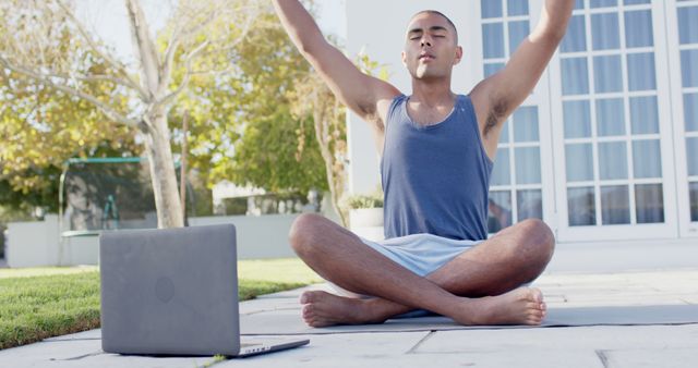 Man practicing yoga outdoors with a laptop. Useful for content related to virtual fitness classes, at-home workouts, mindfulness, and health and wellness tips.