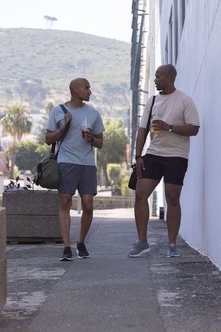 African american men walking and chatting on urban sidewalk holding cold drinks