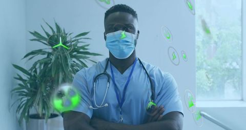Confident male clinician standing arms crossed wearing mask and stethoscope in sunlit clinic