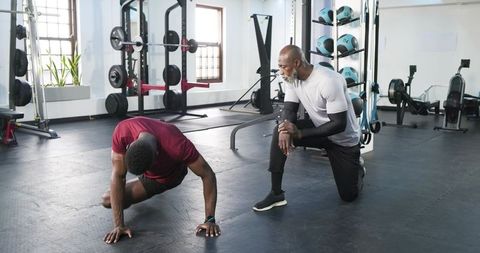 Personal trainer guiding client with push-up in modern gym