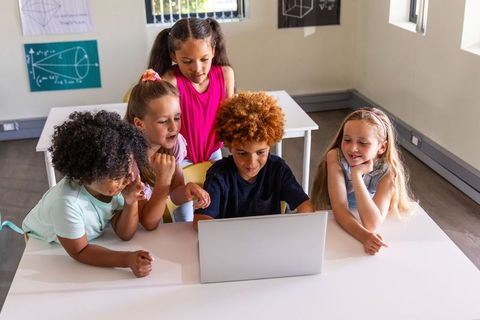 Diverse elementary students collaborating around laptop in bright classroom