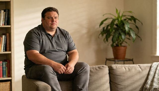 Contemplating middle-aged man sitting on couch clasping hands in cozy living room