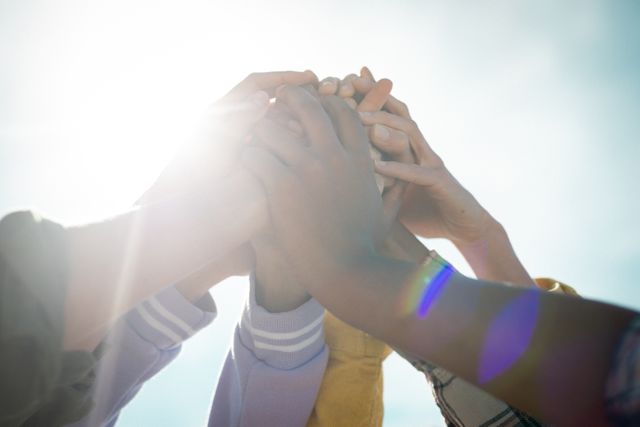 This image shows the hands of diverse female friends coming together in a gesture of unity and support, with bright sunlight in the background. It can be used to represent themes of friendship, teamwork, diversity, and togetherness. Ideal for use in promotional materials for community events, social campaigns, and advertisements focusing on unity and diversity.