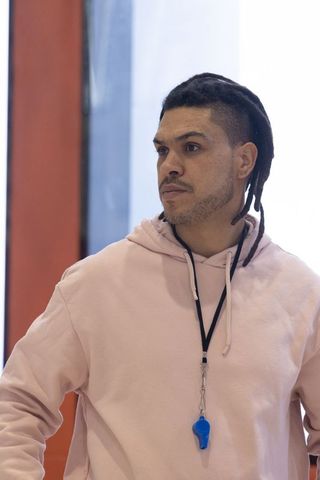 Athletic coach in pink hoodie with blue whistle, inside gym