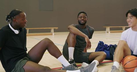 Postgame basketball friends relaxing and laughing on indoor court, teammates bonding