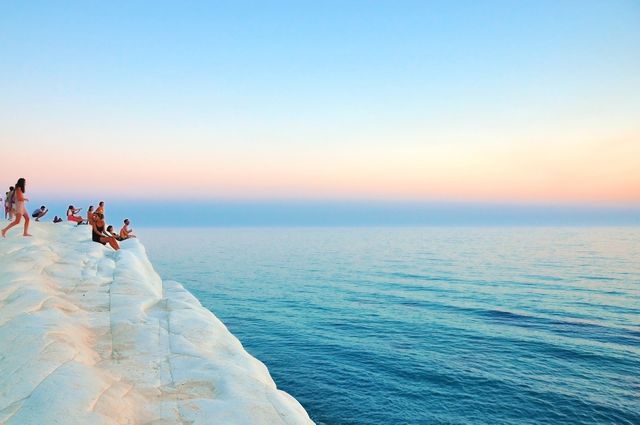 A scenic view of people enjoying the sunset on white cliffs overlooking the sea. The clear sky merges with the horizon, casting warm colors during twilight. This image is perfect for travel blogs, nature websites, or relaxation-themed projects.