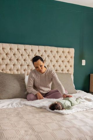 Mother gently caring for newborn on bed with tufted headboard and green accent wall