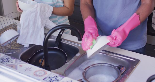 Adult and child washing dishes together in kitchen, focusing on hands doing household chore. Great for articles on family bonding, teaching responsibility, teamwork, domestic life, and promoting cleanliness.