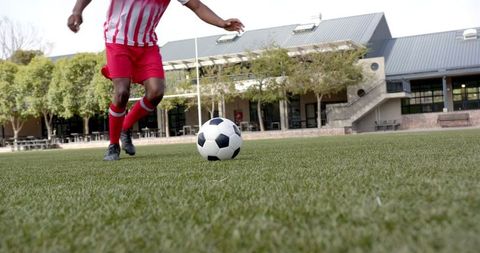 Athlete Dribbling Soccer Ball on Field Near Modern Building