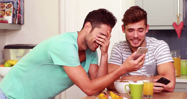 Friends laughing while using smartphones in the kitchen at home