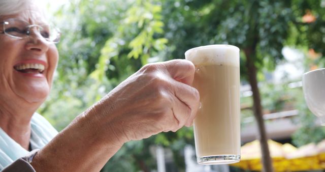 Senior Caucasian woman enjoys a latte outdoors, with copy space. Her smile suggests a moment of relaxation during a pleasant coffee break.