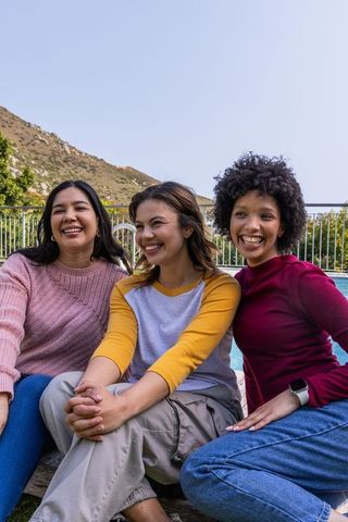 Smiling diverse friends sitting poolside, enjoying sunny casual outdoor friendship