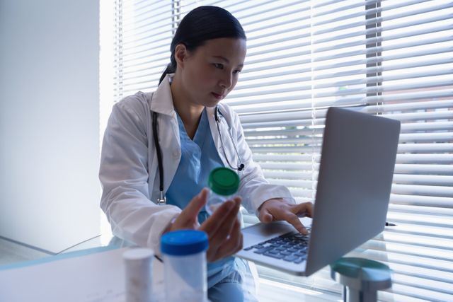 Female doctor holding bottle of pills while using laptop in clinic at hospital  - Download Free Stock Photos Pikwizard.com