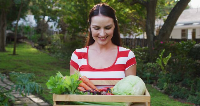 Smiling caucasian woman standing in garden holding box of vegetables. spending free time at home.