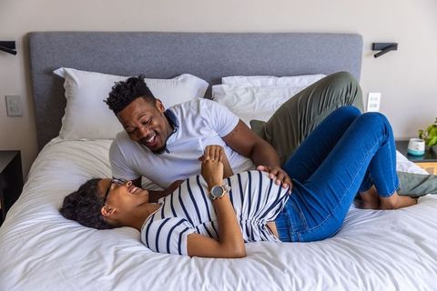 African american expecting couple laughing on bed touching pregnant belly in bedroom