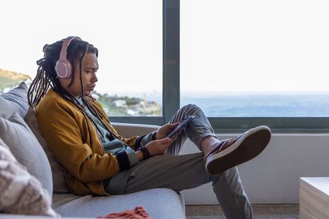 African american man relaxing with pink headphones and tablet by ocean window