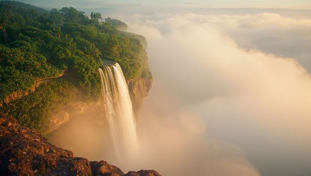 Majestic waterfall cascading into misty valley at sunrise