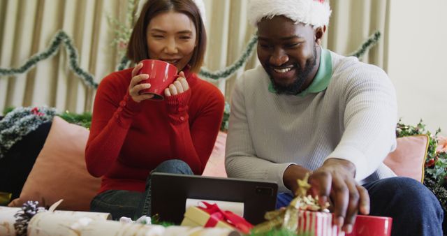 Image of happy diverse couple in santa hats making christmas laptop image call at home. Christmas, celebration, communication, happiness and inclusivity concept.