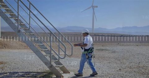 Wind turbine technician walking to staircase wearing safety harness at remote wind farm