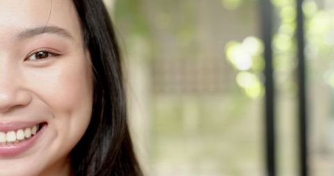 Asian Woman Smiling by Window Overlooking Leafy Garden