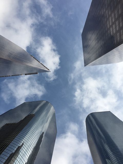 This image shows a perspective view looking up at modern skyscrapers with a blue sky and scattered clouds. Ideal for use in business or urban planning presentations, highlighting modern architecture, or marketing materials for city or travel advertisements.