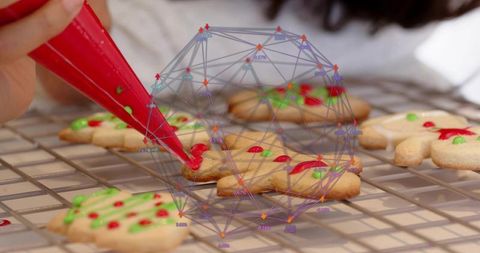Piping red icing on festive cookies on cooling rack with digital wireframe overlay