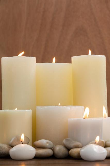 White candles and pebbles arranged on wood background, ideal for promoting spa services, wellness centers, relaxation techniques, and meditation practices. Perfect for use in brochures, websites, and social media posts related to tranquility and self-care.