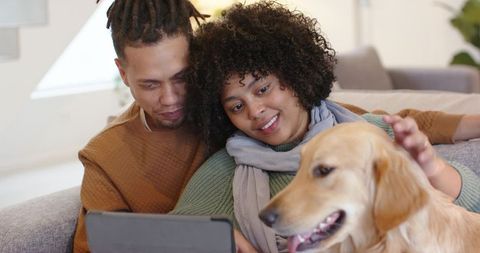 Couple cuddling on couch with golden retriever watching tablet at home