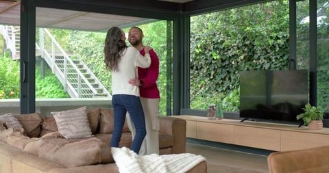 Couple Embracing in Sunlit Modern Living Room with Glass Walls, Sectional Sofa and Garden View